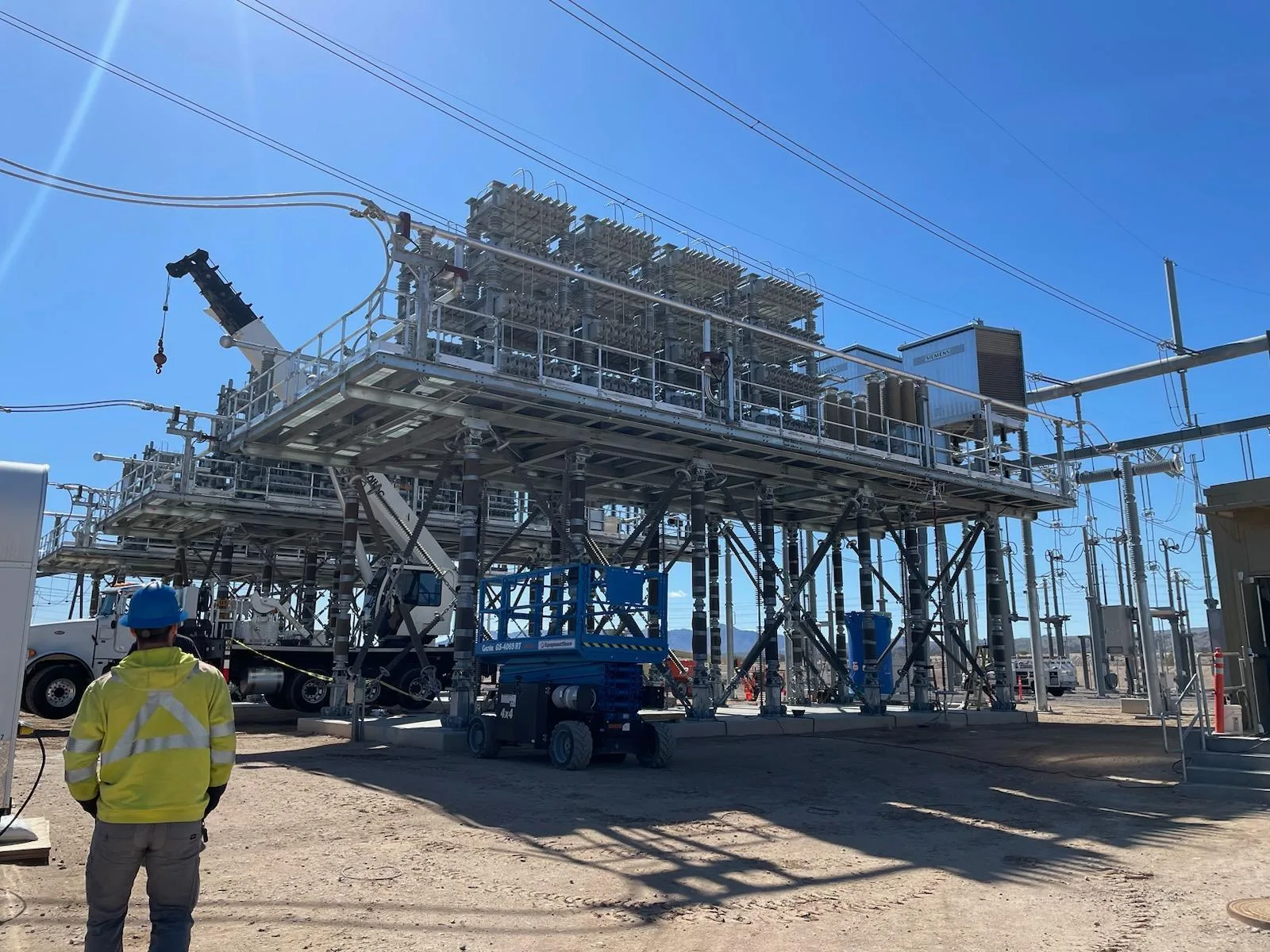 Worker in a hard hat observing a 500 kV capacitor bank installation under a clear sky