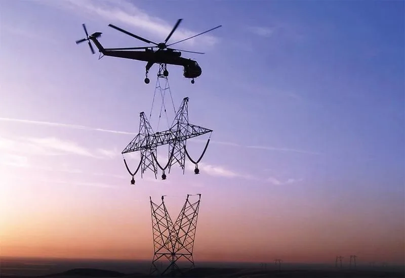 Helicopter lowering a 230 kV transmission tower section at sunset